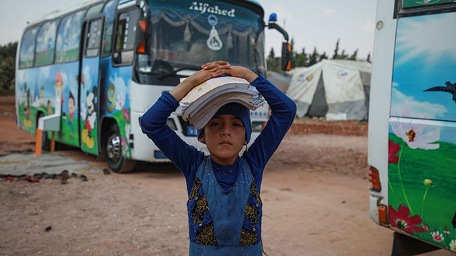 فتاة سورية نازحة تحمل كتبًا على رأسها 